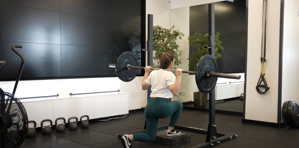 Woman performing deficit reverse lunge with barbell