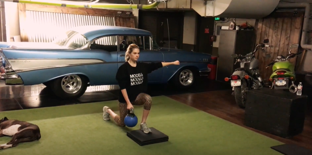 Woman doing deficit reverse lunge with kettlebell in the garage