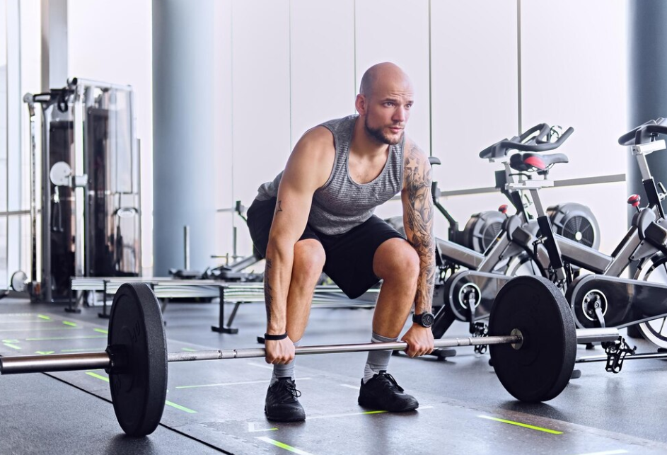 bearded shaved head male working out with a barbell in a gym club